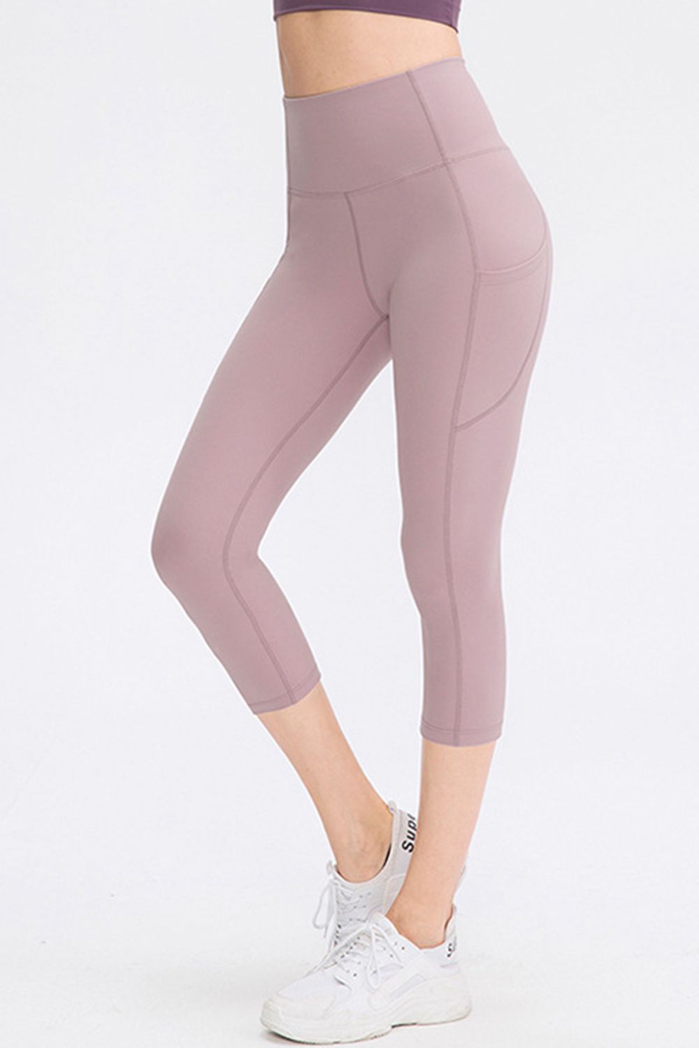 Person wearing mauve leggings and white sneakers on a white background