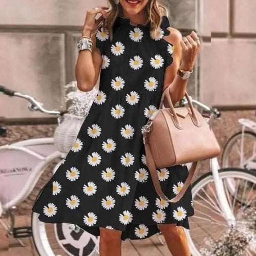 Woman wearing a black dress with white floral patterns, holding a pink handbag, standing in an urban setting with bicycles.