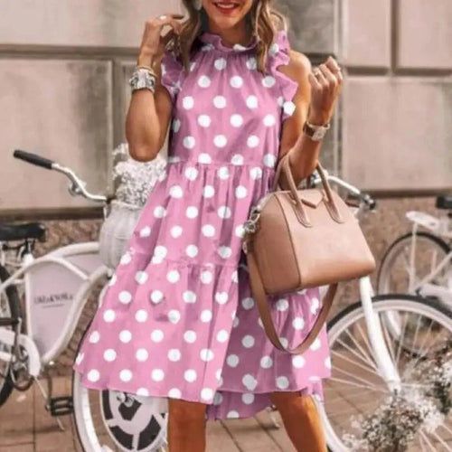 Woman in a pink polka dot dress holding a beige handbag with bicycles in the background.
