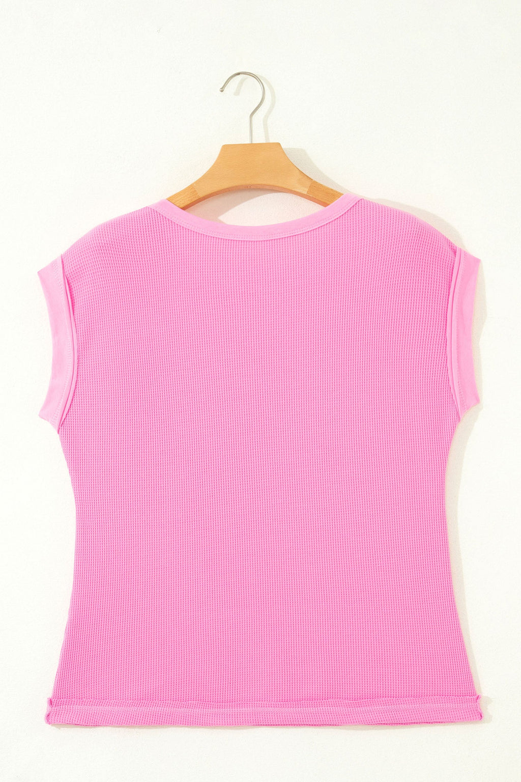 Pink sleeveless top on a wooden hanger against a white background