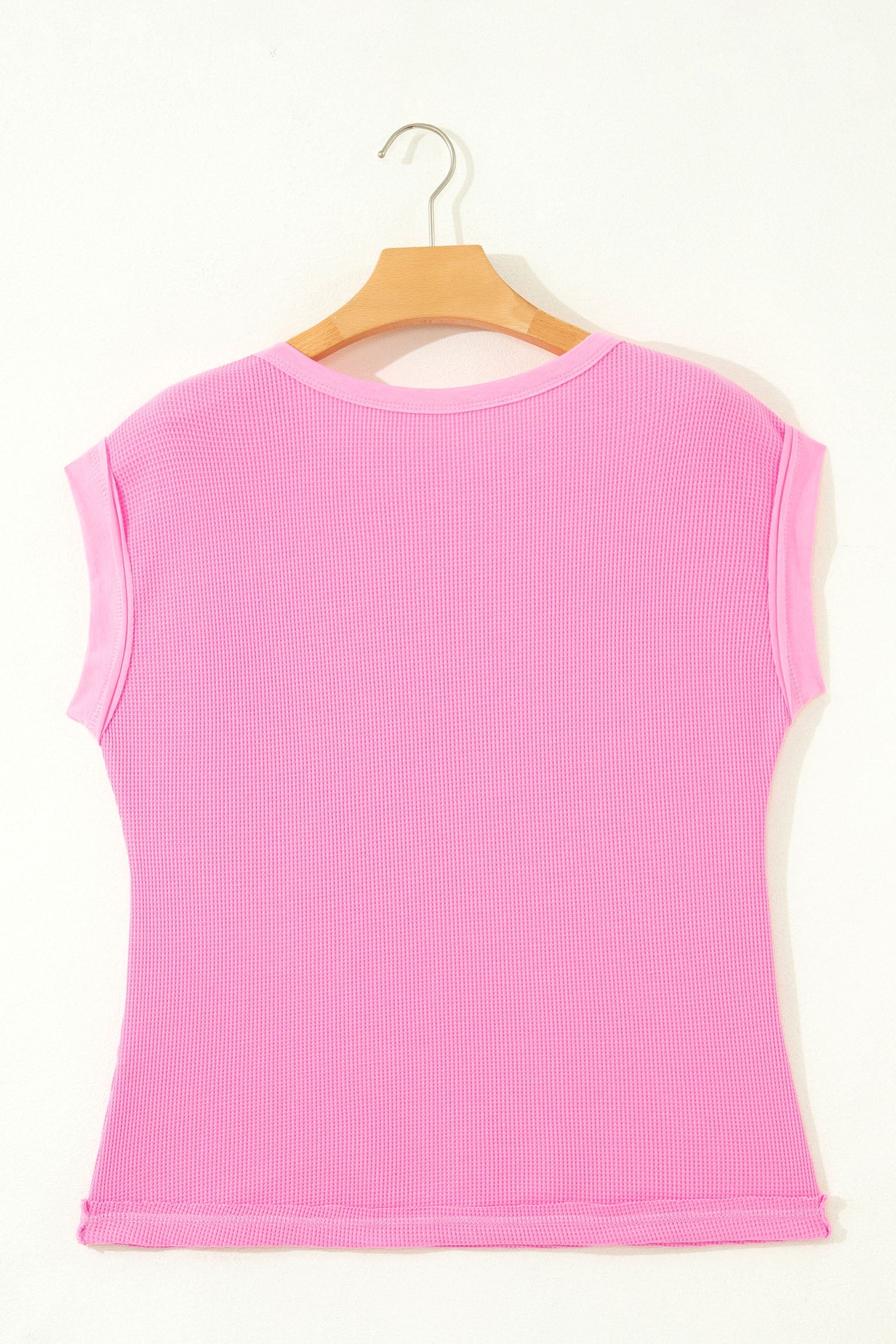 Pink sleeveless top on a wooden hanger against a white background