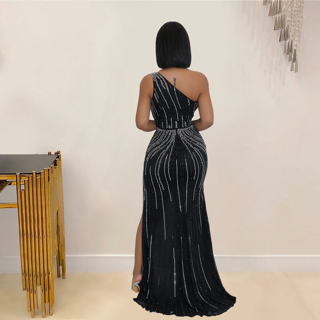 Woman wearing a black one-shoulder evening gown with silver beading in a room.