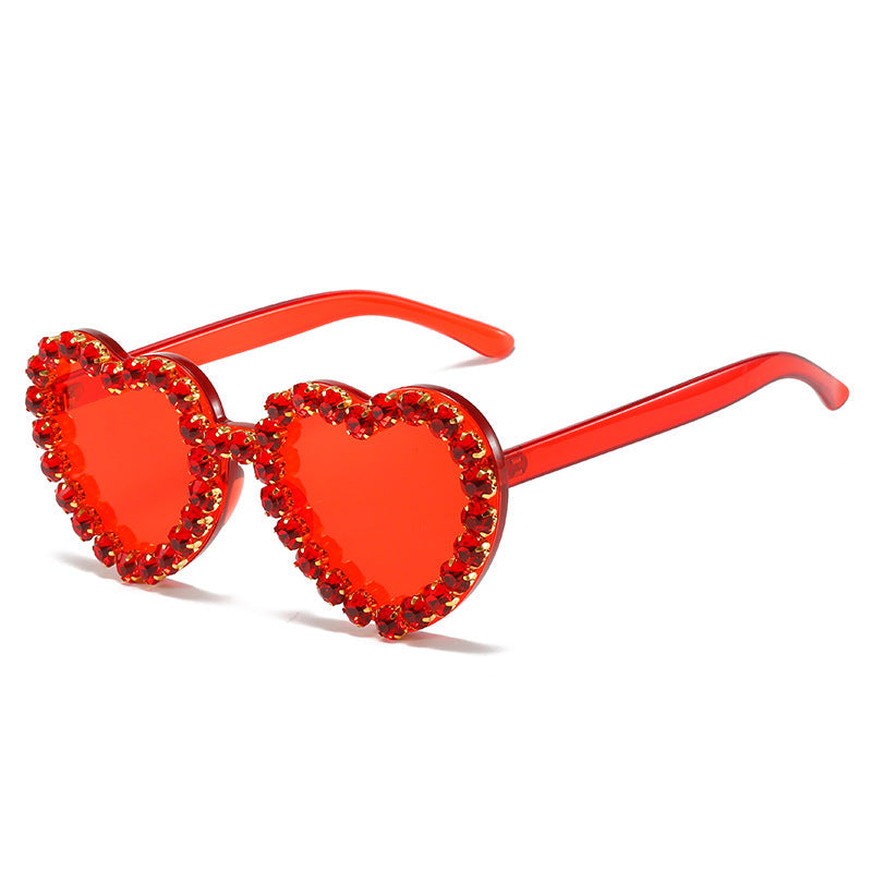 Heart-shaped sunglasses with red lenses and embellishments on a white background