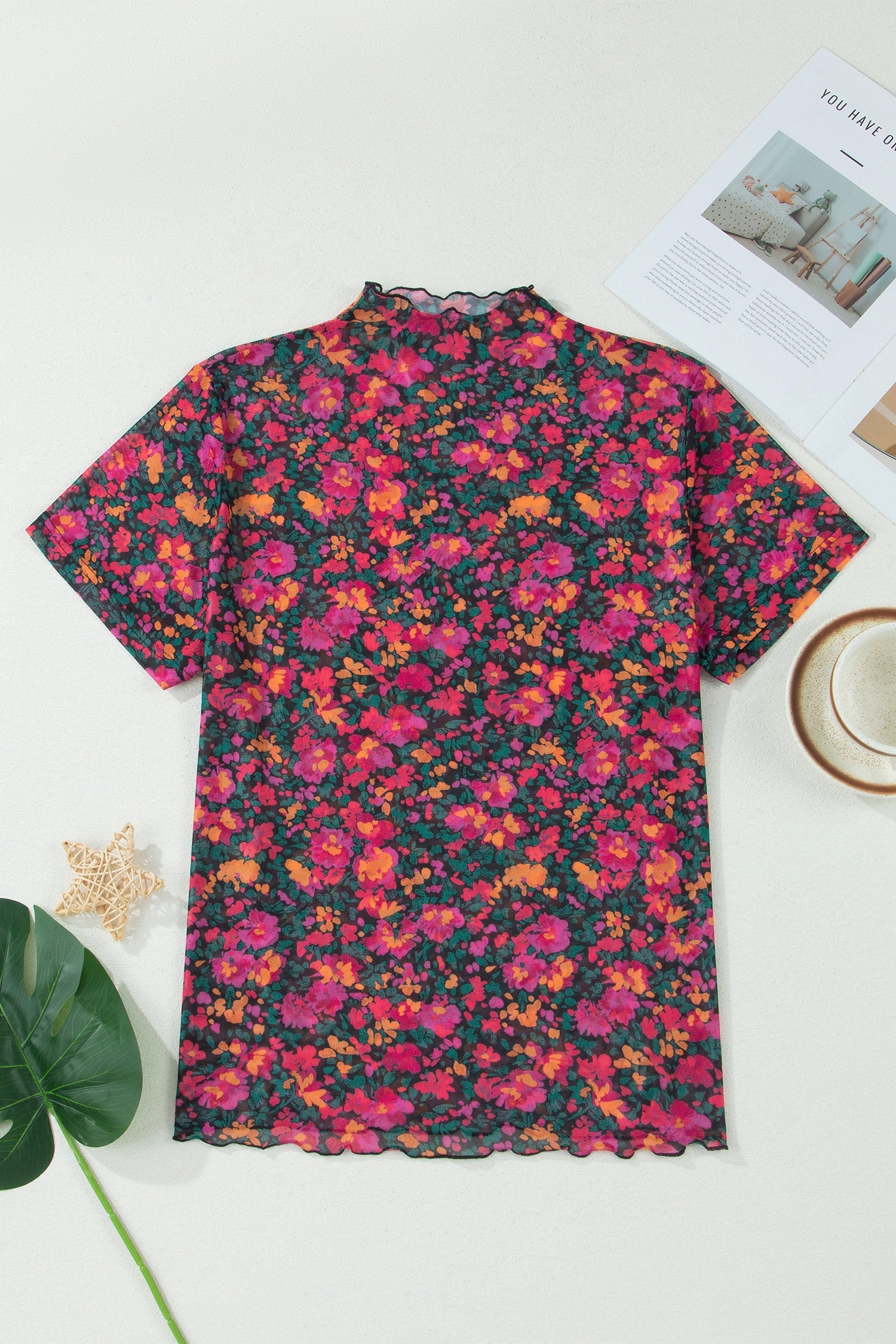 Floral patterned shirt on a white surface with a cup and magazine.