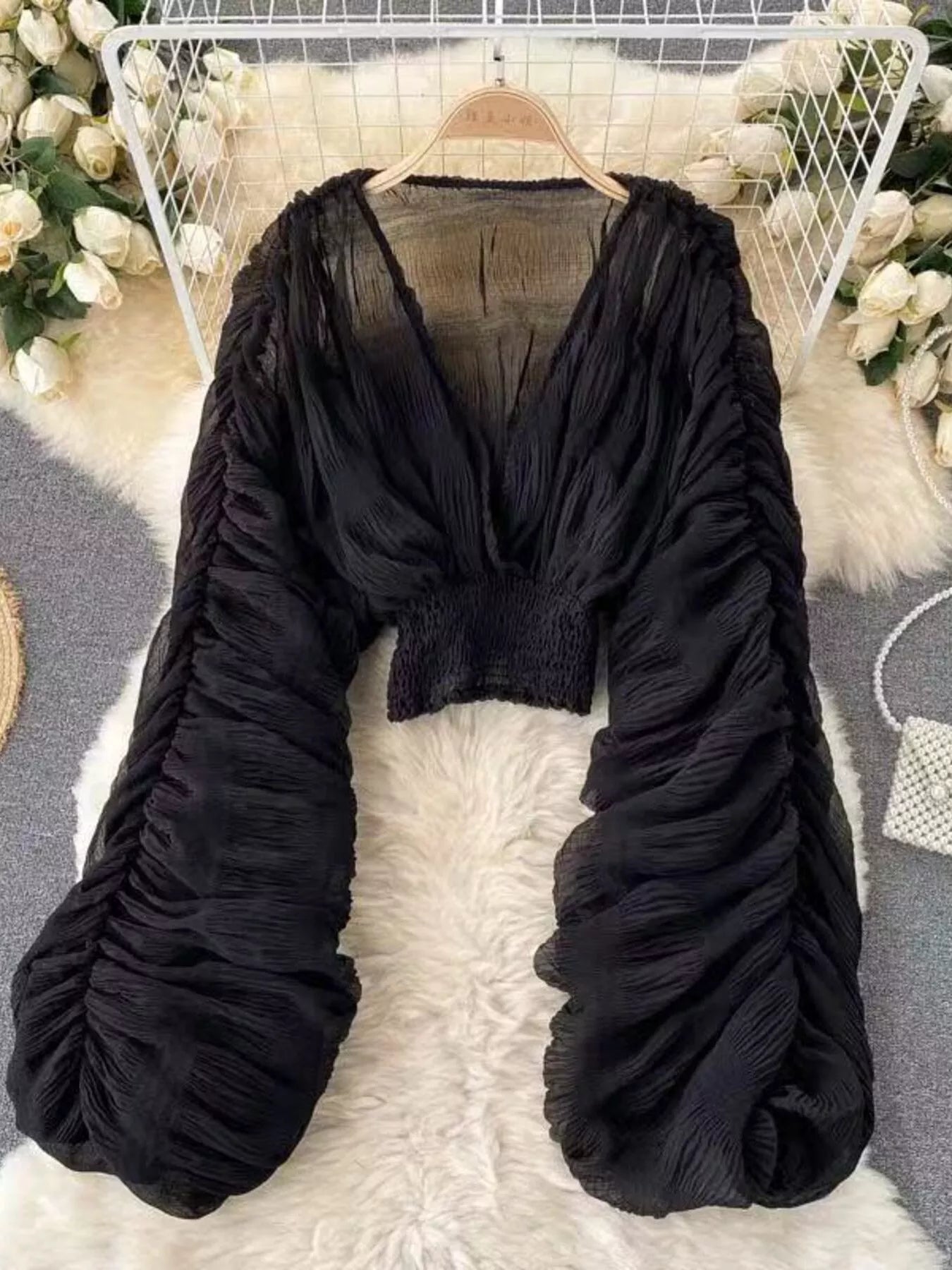 Black ruched top on a hanger with floral decorations in the background