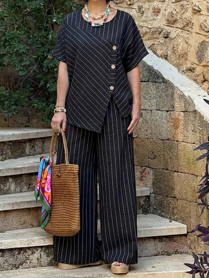 Person wearing a black pinstripe outfit with a woven bag, standing on stone steps.