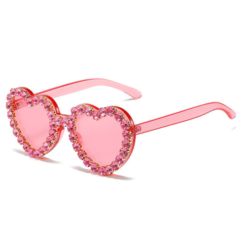 Heart-shaped sunglasses with pink lenses and embellishments on a white background