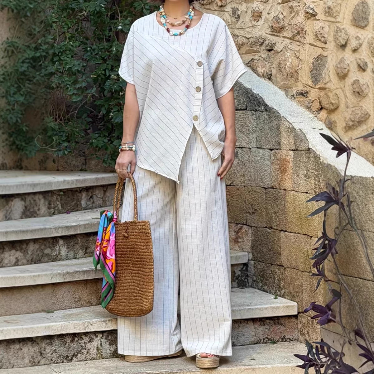 Person wearing a white outfit with a textured top and wide-leg pants, standing on stone steps.