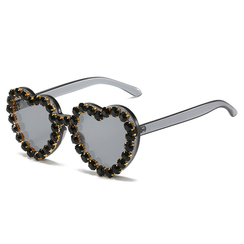 Heart-shaped sunglasses with dark brown rhinestone-studded frames and translucent gray temples, shown on a clean white background.