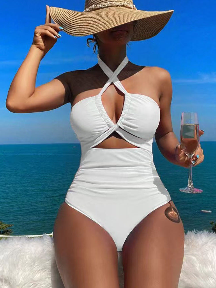 Woman in a white swimsuit and sun hat holding a glass of pink champagne by the ocean.