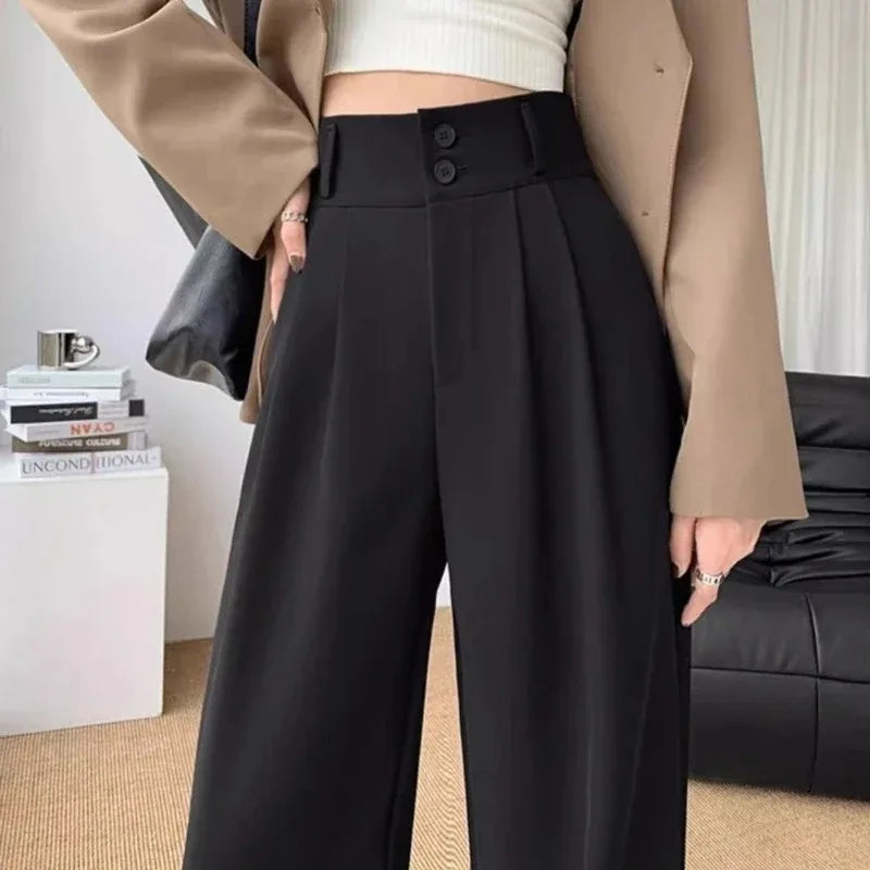Person wearing black high-waisted pants with a beige jacket indoors.