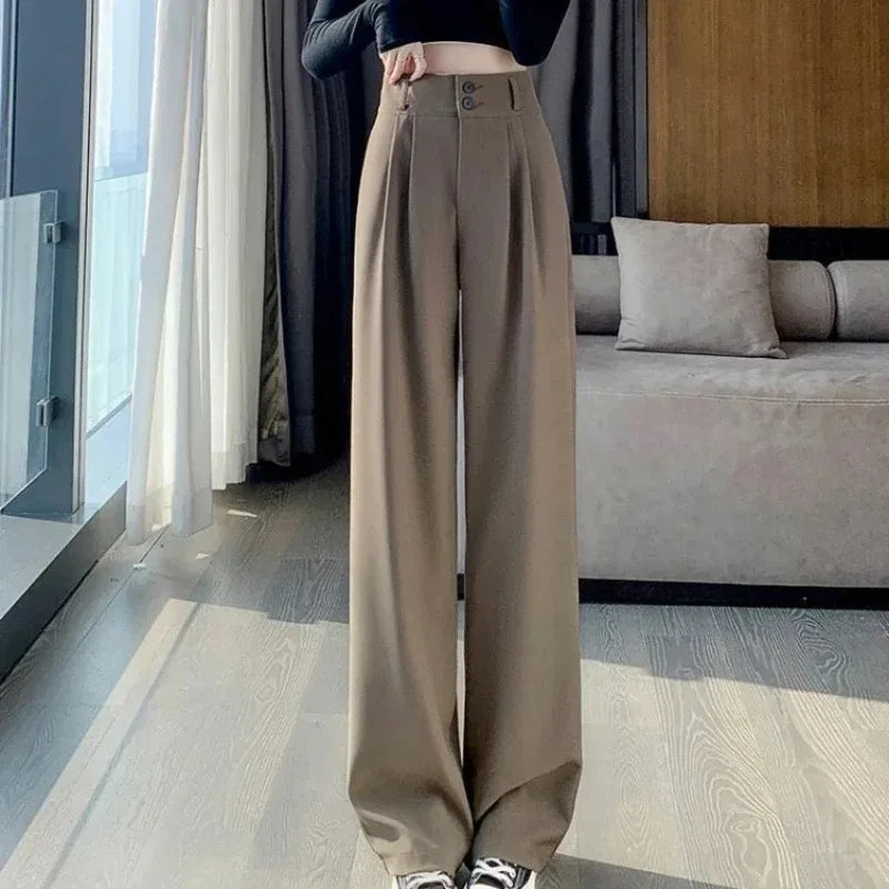 Person wearing beige high-waisted pants in a room with a bed and large window.