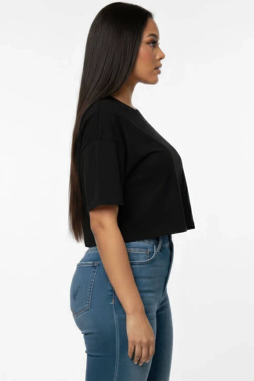 Woman wearing a black crop top and blue jeans on a white background showing side View