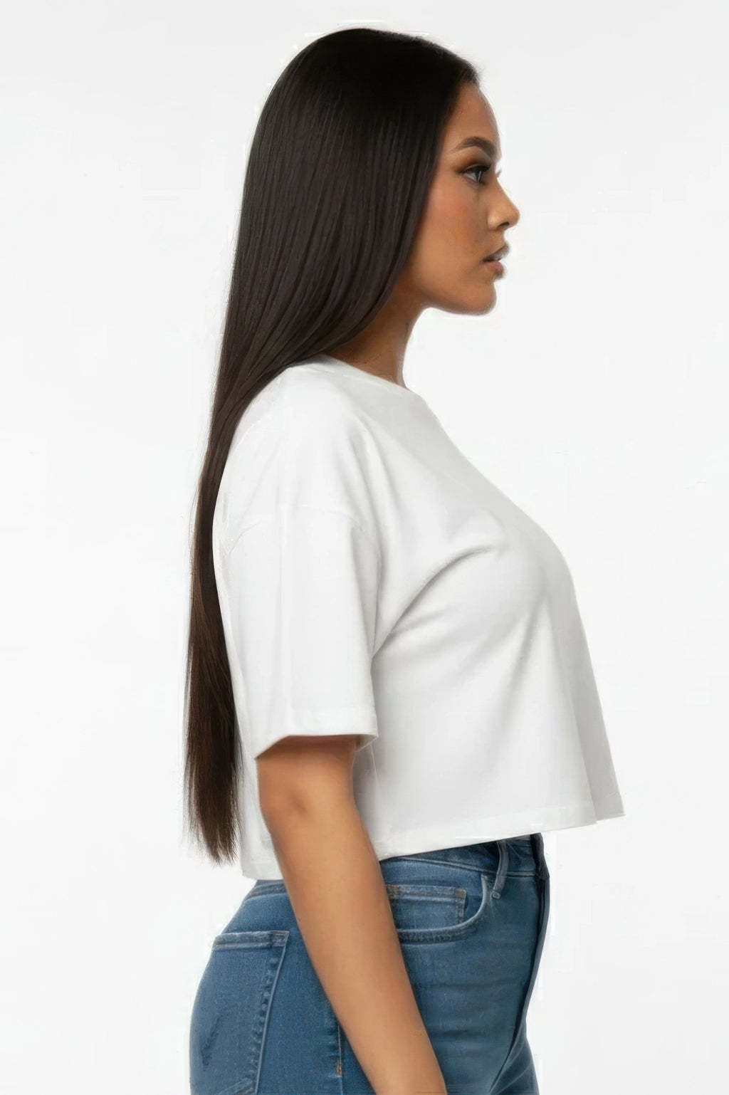 Woman wearing a white crop tshirt and blue jeans on a plain background. Showing the side of the tshirt. 