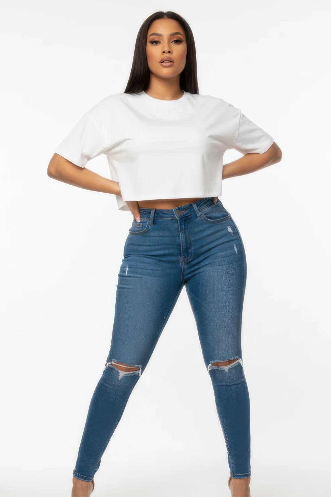 Woman wearing a white cropped top and blue ripped jeans on a white background