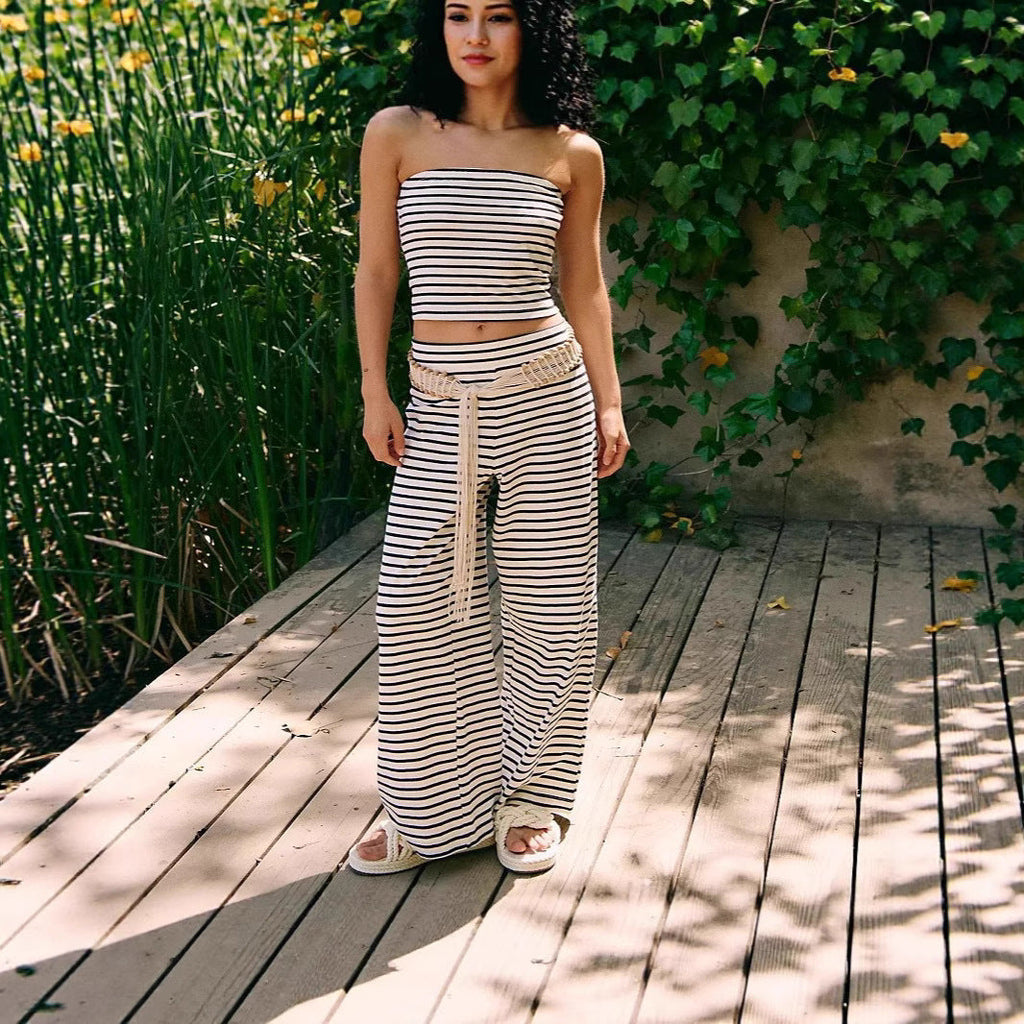 Woman in a striped outfit standing on a wooden deck with greenery in the background