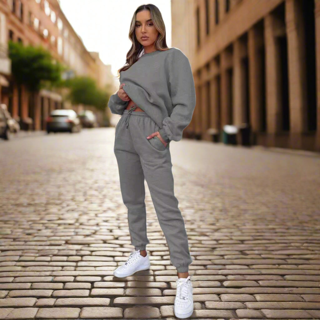 Woman in a gray tracksuit standing on a cobblestone street.