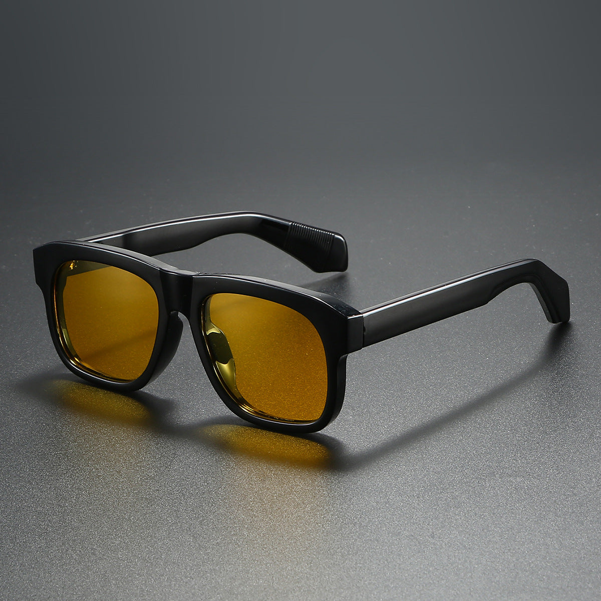 Black-framed sunglasses with yellow lenses on a gray background