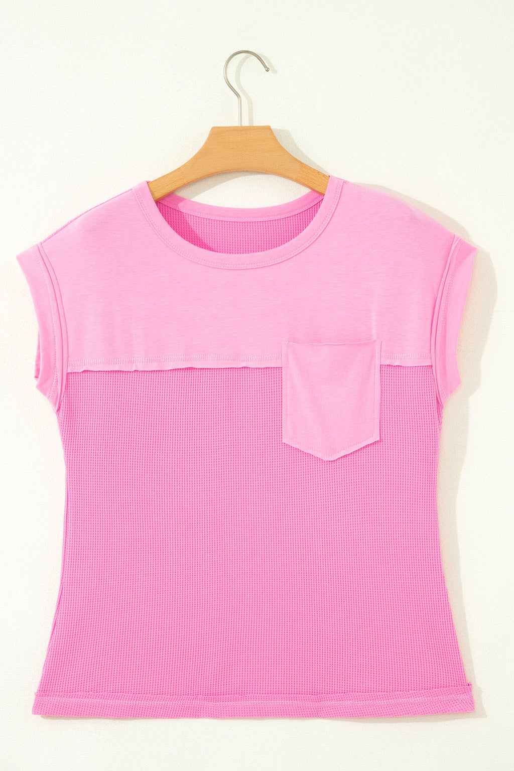 Pink sleeveless top with a pocket on a wooden hanger against a white background