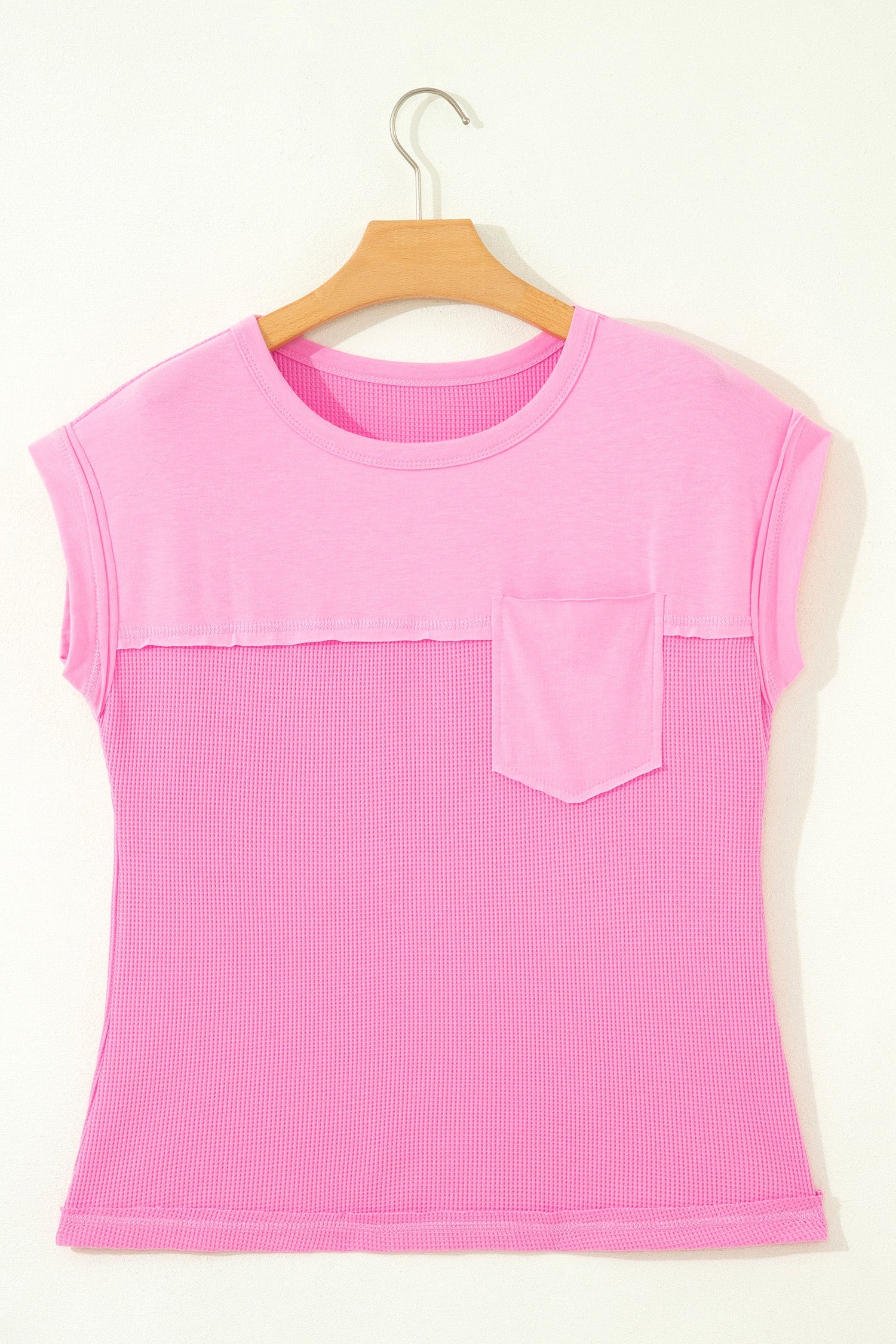 Pink sleeveless top with a pocket on a wooden hanger against a white background