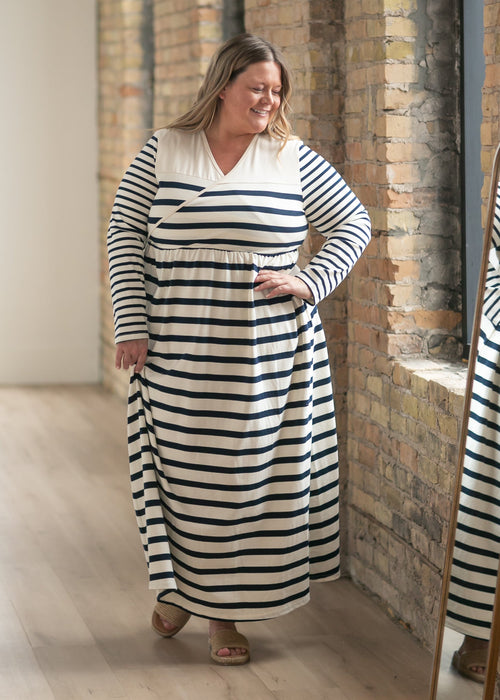 Woman wearing a black and white striped dress standing in a room with brick walls.