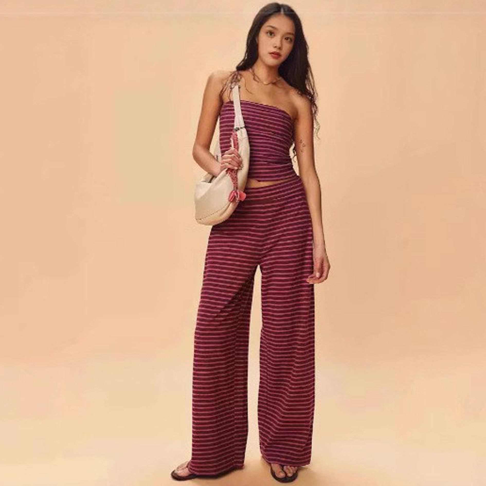 Woman wearing a striped outfit with a beige bag on a peach background