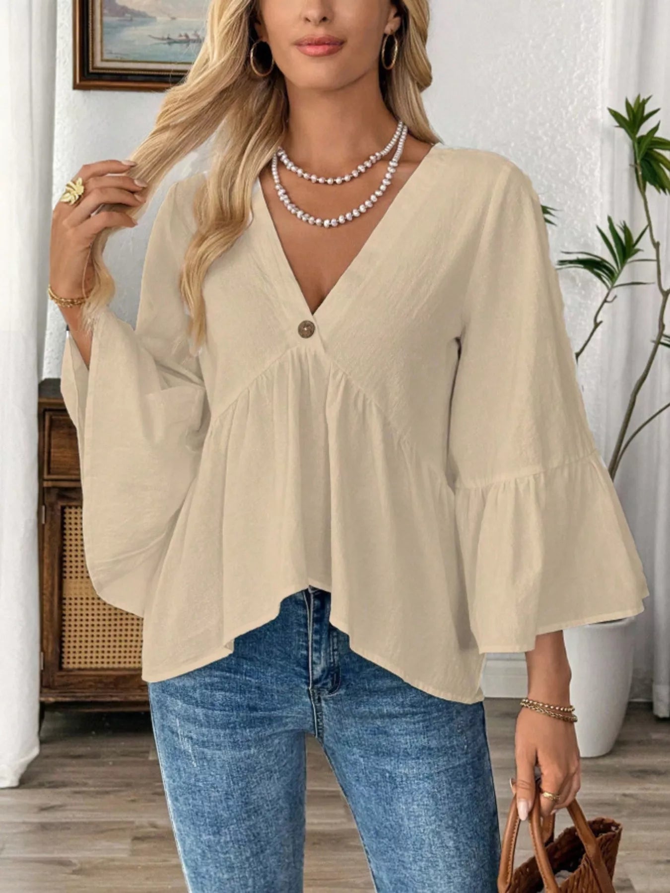 Woman wearing a beige blouse and blue jeans indoors.