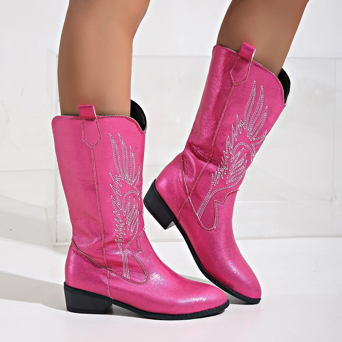 Pink cowboy boots with wing designs on a white background