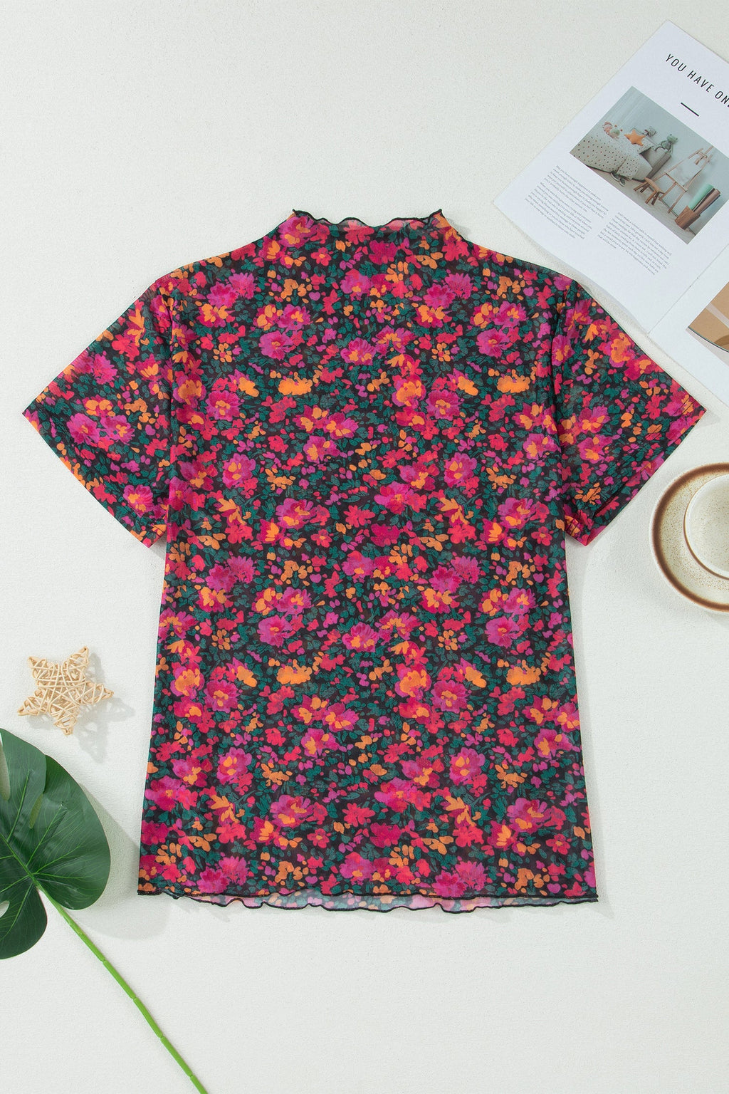 Floral patterned shirt on a white surface with a cup and magazine in the background