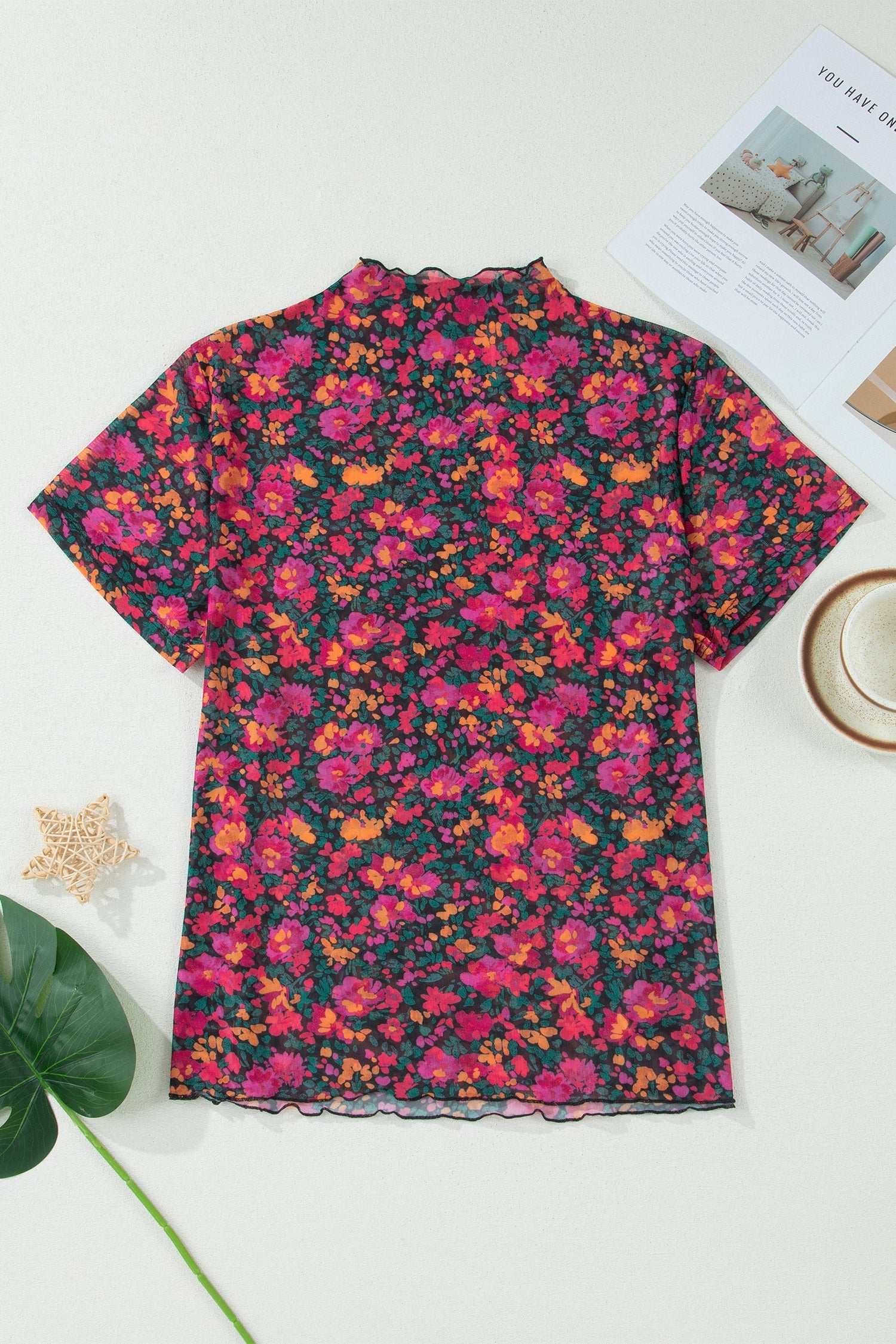 Floral patterned shirt on a white surface with a cup and magazine in the background