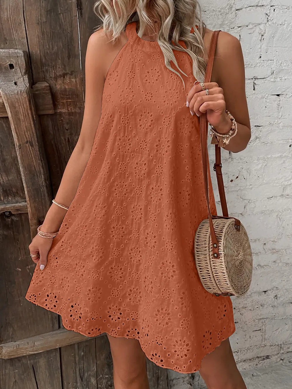 Woman wearing a rust-colored dress holding a round wicker bag against a rustic wooden and brick wall.