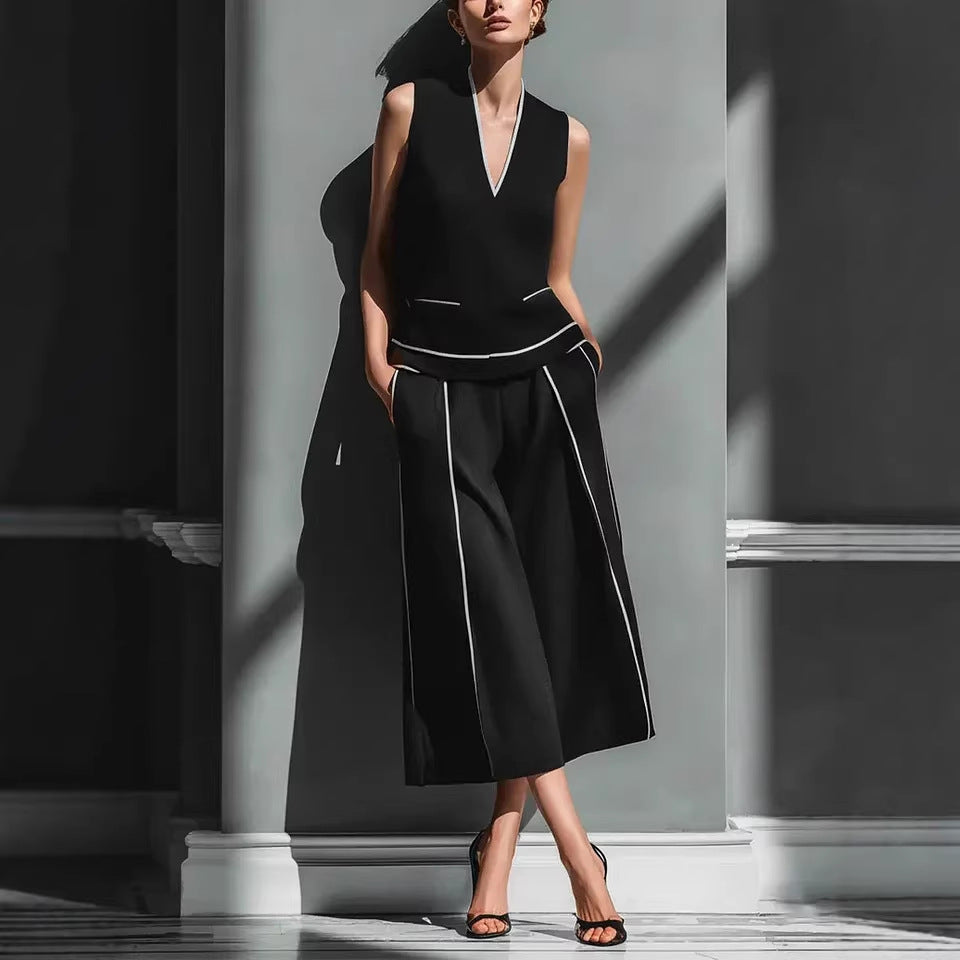 Woman wearing a black sleeveless top and wide-leg pants with white piping in a minimalistic setting.