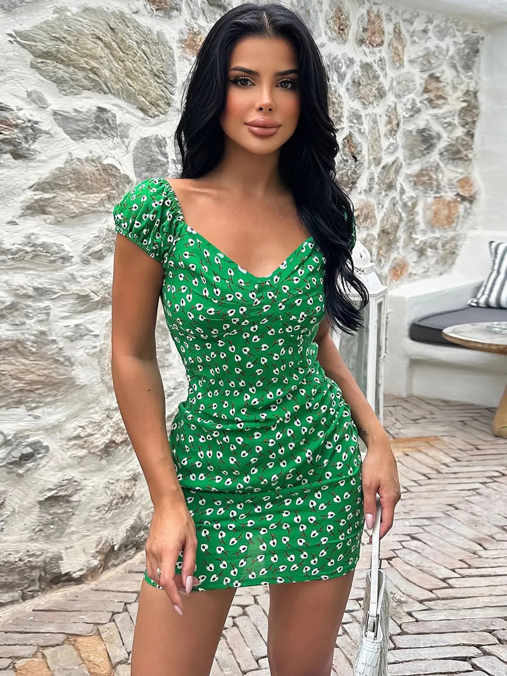 Woman in a green floral dress standing against a stone wall.